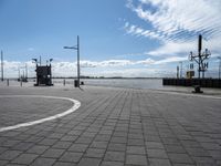 a parking area at the edge of a wide river near some poles and lights and a clock