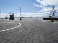 a parking area at the edge of a wide river near some poles and lights and a clock