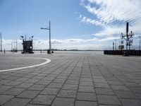 a parking area at the edge of a wide river near some poles and lights and a clock