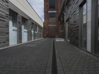 two rows of concrete buildings along an empty sidewalk with metal ventilation systems lining both sides and a brick structure