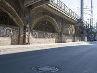 graffiti covered brick wall and gate under an overpass in an urban area with sun light