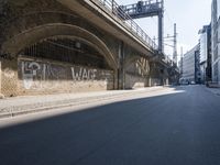 graffiti covered brick wall and gate under an overpass in an urban area with sun light