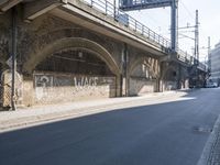 graffiti covered brick wall and gate under an overpass in an urban area with sun light