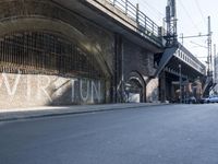graffiti covered brick wall and gate under an overpass in an urban area with sun light