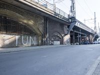 graffiti covered brick wall and gate under an overpass in an urban area with sun light