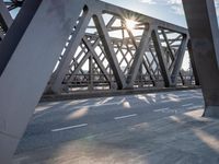 a skateboarder riding across a bridge under some large beams while the sun is setting
