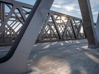 a skateboarder riding across a bridge under some large beams while the sun is setting