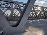 a skateboarder riding across a bridge under some large beams while the sun is setting