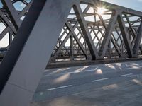 a skateboarder riding across a bridge under some large beams while the sun is setting