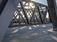 a skateboarder riding across a bridge under some large beams while the sun is setting