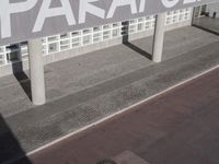 a view of a sidewalk with several pillars and a building in the background with text on it