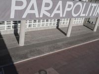 a view of a sidewalk with several pillars and a building in the background with text on it