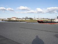 a man riding a skateboard down a paved area next to water with boats in background