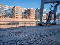 a person that is walking on brick pavement near water and buildings with a bridge in the background