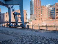 a person that is walking on brick pavement near water and buildings with a bridge in the background