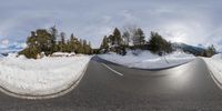 fish eye lens panoramic photograph of a road with evergreens and snow covered hillside