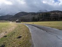 a empty road leading towards an idyllic village and mountains in the distance,