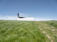 an outdoor house is set on the hill of grass and plants in a field with an open sky background