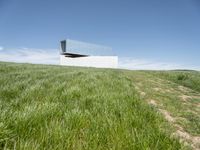 an outdoor house is set on the hill of grass and plants in a field with an open sky background