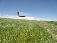 an outdoor house is set on the hill of grass and plants in a field with an open sky background