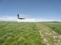 an outdoor house is set on the hill of grass and plants in a field with an open sky background