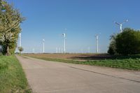 a dirt road with wind generators on each side near a green field and a fenced off area with an area for corn