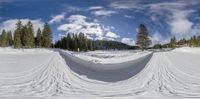 a wide angle shot of snow covered area at a ski resort with skiers in the background