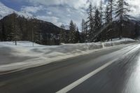 the highway is covered in snow with mountains in the background and trees on both sides