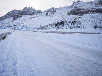 a snow covered mountain road with rocks in the distance and a bench on the right side