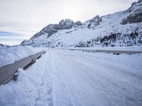 a snow covered mountain road with rocks in the distance and a bench on the right side