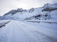 a snow covered mountain road with rocks in the distance and a bench on the right side