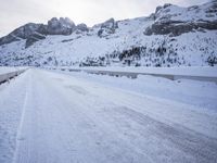 a snow covered mountain road with rocks in the distance and a bench on the right side