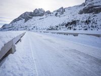 a snow covered mountain road with rocks in the distance and a bench on the right side