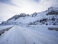 a snow covered mountain road with rocks in the distance and a bench on the right side