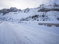 a snow covered mountain road with rocks in the distance and a bench on the right side