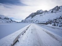 a snow covered mountain road with rocks in the distance and a bench on the right side