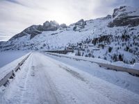 a snow covered mountain road with rocks in the distance and a bench on the right side