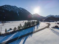 a highway runs past snowy mountains in a valley, with sun peeking over top of the mountain