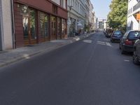 there are several cars parked at the curb of this side street where cars are parked, the buildings have shops on either sides