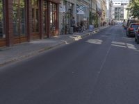 there are several cars parked at the curb of this side street where cars are parked, the buildings have shops on either sides