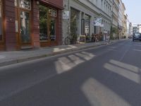 there are several cars parked at the curb of this side street where cars are parked, the buildings have shops on either sides