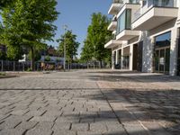 a paved courtyard in front of an office building near a park filled with benches and trees