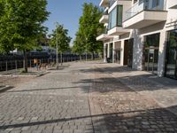 a paved courtyard in front of an office building near a park filled with benches and trees