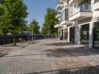 a paved courtyard in front of an office building near a park filled with benches and trees