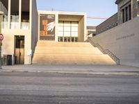 the large, empty sidewalk with multiple columns in front of the building with two signs