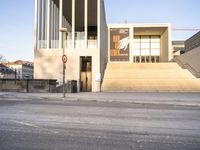 the large, empty sidewalk with multiple columns in front of the building with two signs