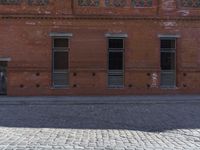 the small child is standing in front of the red building near the brick streetlight