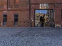 the small child is standing in front of the red building near the brick streetlight