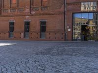 the small child is standing in front of the red building near the brick streetlight