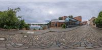 a fisheye image of a brick road with parked bikes and buildings in the background